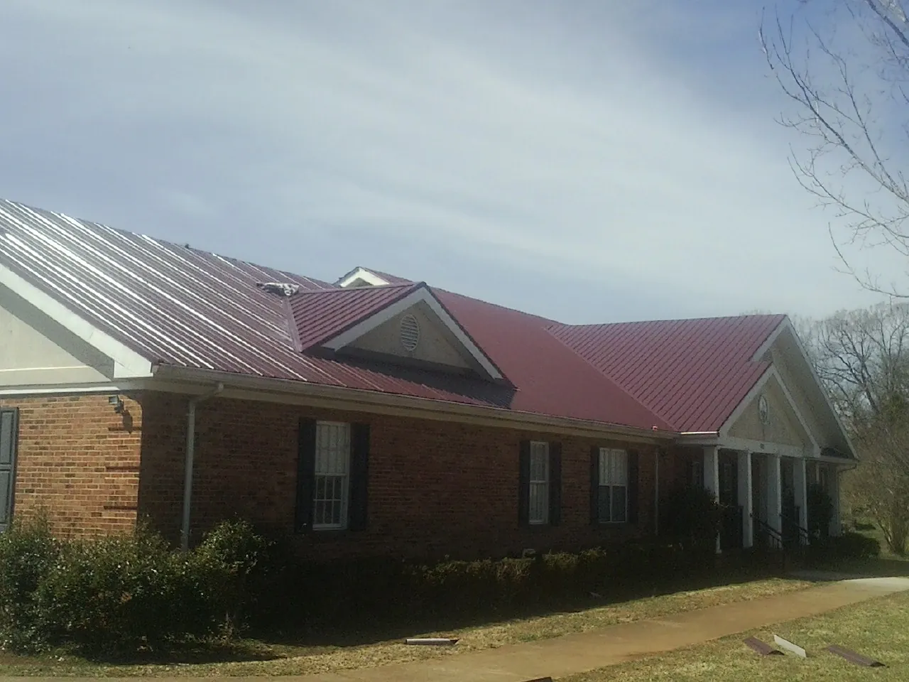 Red metal roof with gabled entries on a long brick building, from a Hail Damage Roof Repair job in Merrill