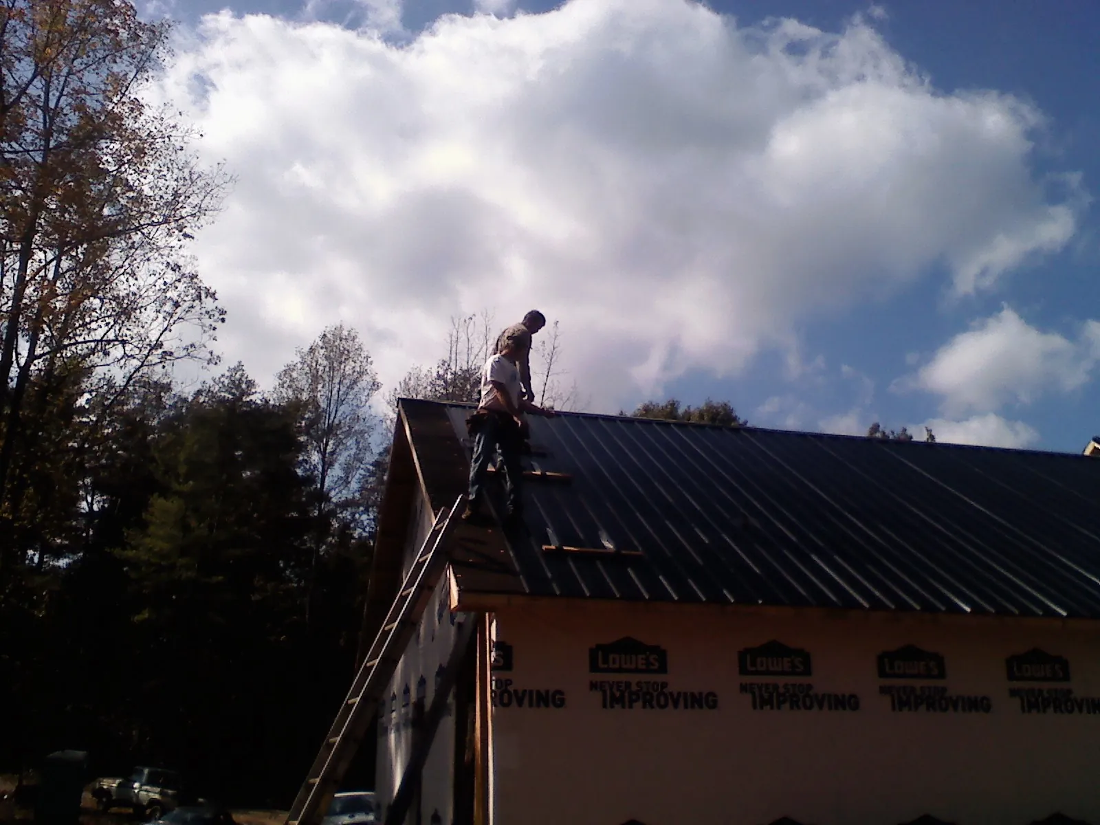 Roofer fastening dark metal panels high against a cloudy sky, from a Roof Inspection job in Merrill